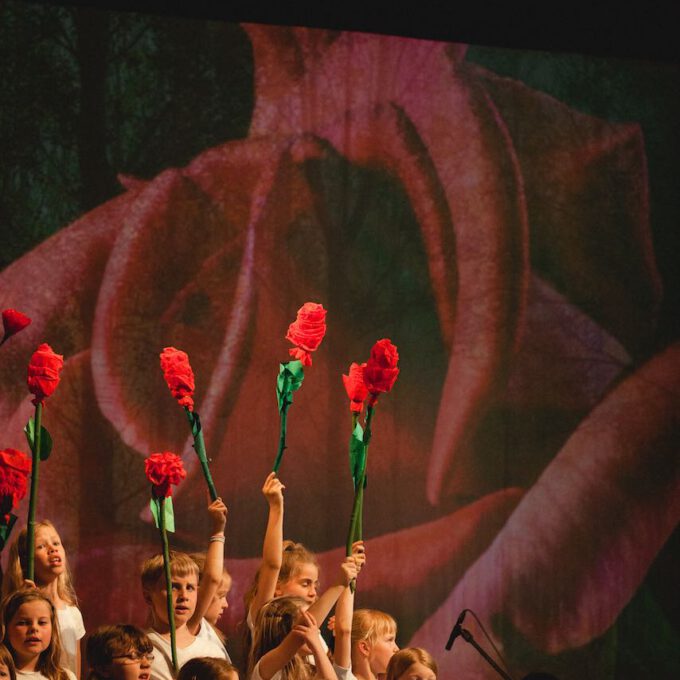Mitglieder des Kinderchores halten selbstgebastelte Rosen in den Händen, im Hintergrund die Projektion einer großen Rosenblüte
