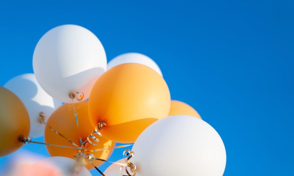Weiße und orangefarbene Luftballons vor blauem Himmel