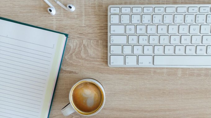 Schreibtisch mit Kaffee, Tastatur, Notizblock und Kaffee